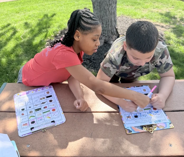 Two students work together on nature-walk checklists at an outdoor picnic table